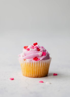 Pembe kremalı ve beyaz arka planda kalpleri olan bir cupack kap..