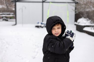 Kışlık ceketli çocuk kartopu atmaya hazırlanıyor.