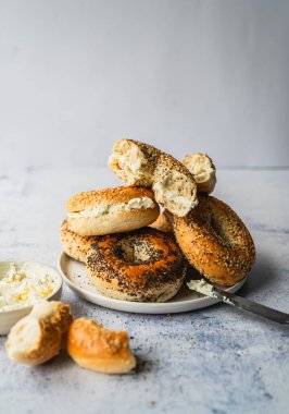 Açık arkaplanda krem peynirli çeşitli simit tabağı.