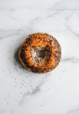 Beyaz mermer arka planda tek haşhaş tohumlu simit üst görünümü.