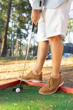 Stylish man in white shorts and suede shoes holding mini golf club clipart