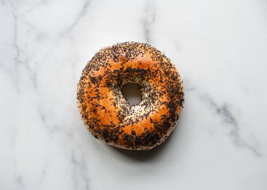 Beyaz mermer arka planda tek haşhaş tohumlu simit üst görünümü.