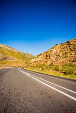 Dönek yol, dağlar, bitki örtüsü, mavi gökyüzü, güneş ışığı.