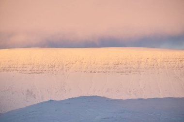 Pastel pembe gün doğumu kışın karlı dağ sıralarını aydınlatıyor.