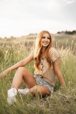 Dağın eteklerinde kızıl saçlı mutlu bir kadın parlıyor.