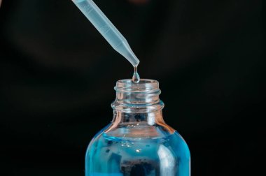 Mavi serumu cam bir şişeye boşaltan bir damlacının yakın çekimi.