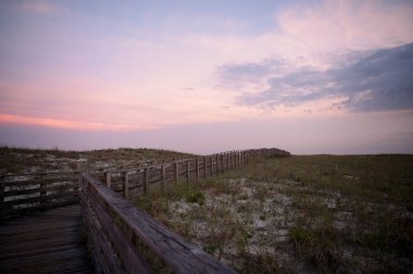 Pastel bir günbatımı gökyüzünün altında sahil kumullarında tahta tahta kaldırım.