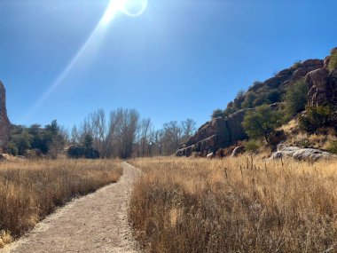 Güneşli toprak yol kayalık kayalıklarla kuru otlaklarda dönüyor.