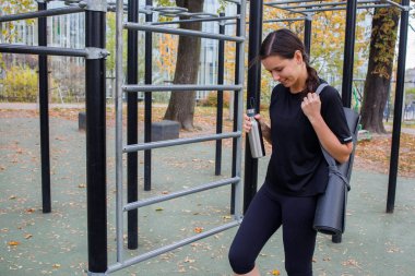 Eğitimden önce parkta yoga minderi ve şişesi olan bir kız.
