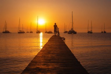 Gün batımı sahnesi, iskeledeki bisikletli adam silueti.