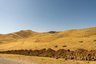 Arka planda mavi gökyüzü olan çorak, kayalık bir çöl manzarası.