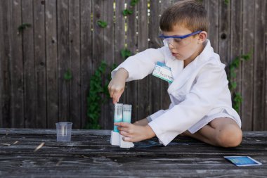 Laboratuvar önlüklü ve gözlüklü genç bir bilim deneyi yapıyor.