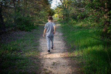 Genç bir çocuk elinde sopayla ormanda tek başına yürüyor.