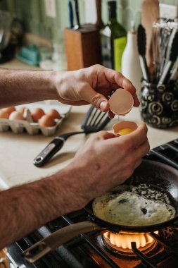Kimliği belirsiz bir adam gaz ocağında sıcak bir tavaya yumurta kırıyor.