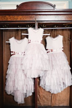 Üç fırfırlı pembe çiçekli kız elbisesi eski moda bir savaşta asılı duruyor.