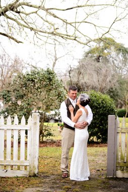 Gelin ve damat kırsal bir çitin yanında kucaklaşıyor.