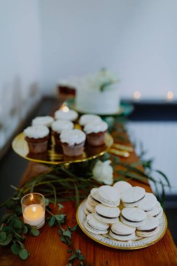 Makaronlar, kekler ve mum dekoru olan zarif bir tatlı masası.