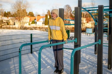 Genç bir kadın kışın açık havada paralel barlarda egzersiz yapıyor..