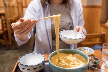 Lokantada yemek çubuklarıyla bir kase körili udon kaldırılıyor.