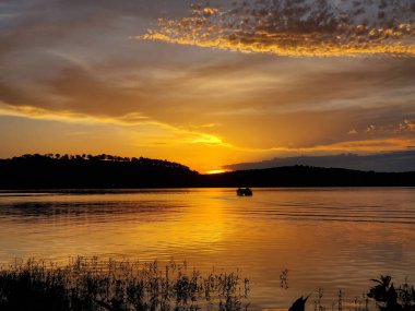 Gün batımında altın bir gölde, dalgalı suyla silueti olan bir tekne.