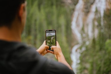 Canmore, Alberta 'da bir şelalenin fotoğrafını çeken genç adam.