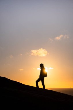 Sırt çantalı yürüyüşçünün silueti altın gün batımında bir tepede duruyor.