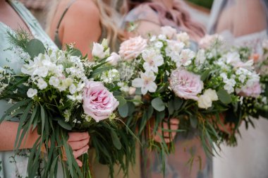 Beyaz ve pembe gül buketleri ve kır çiçekleri tutan nedimeler.