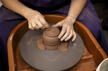 Potter, tekerleğin üzerinde süngerle dönen bir kil parçasını düzeltiyor.