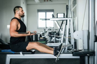 Modern bir spor salonunda, kablo sırası makinesinde atletik adam eğitimi.
