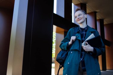 Genç kızıl kız modern binanın yakınında mutlu bir gelecek arıyor.