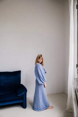 Yumuşak mavi örgü süveterli, sakin, düşünceli bakışlı bir kadın..