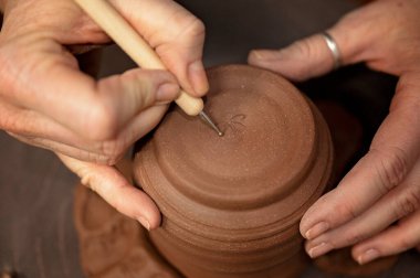 Potter, detayları dönen bir kil parçasına kazımak için bir araç kullanıyor