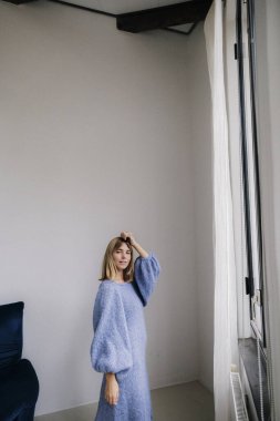 Yumuşak mavi örgü süveterli, sakin, düşünceli bakışlı bir kadın..