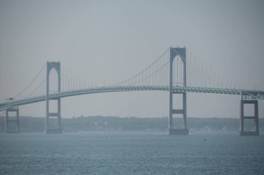 Sisli bir sahil gününde asma köprü su boyunca uzanır.