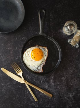 Üst manzara tavada pişmiş yumurta ve siyah arka planda tabak çatal bıçak takımı..