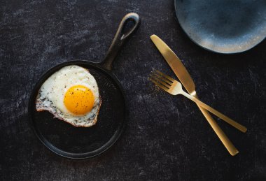 Üst manzara tavada pişmiş yumurta ve siyah arka planda tabak çatal bıçak takımı..