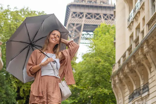 Paris 'te Eyfel Kulesi' nin yanında şemsiyeyle yürüyen bir kadın.
