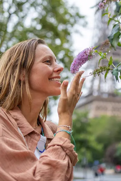 Gülümseyen kadın mor çiçeğin kokusundan zevk alıyor.