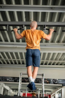 Modern bir spor salonunun barında barfiks çeken bir adam.