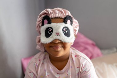 Saç bonesi ve göz maskesi takmış, uyku kıyafetleriyle melez bir genç kız.