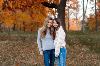 Anne ve ergen kız, sonbahar günü güzel bir parkta yan yana dururlar.
