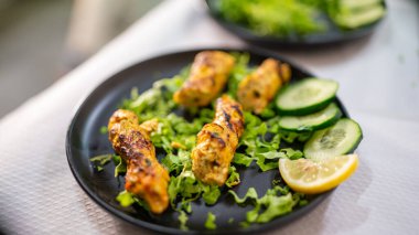 Siyah tabakta salata ve salatayla servis edilen tavuk şiş kebap.
