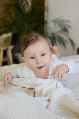 Evdeki yumuşak beyaz battaniyeye uzanmış gülümseyen bebek.