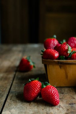 Eski bir masada, ahşap bir sepetin içinde taze çilekler..