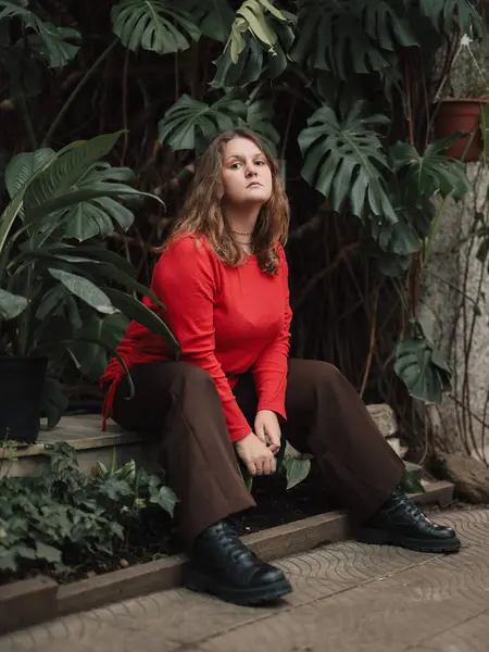 Kırmızılı genç kadın yemyeşil bitkilerin arasında oturuyor.