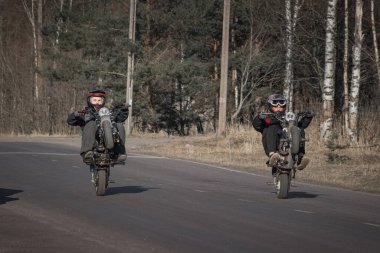15 yaşındaki kasklı çocuklar kırsal bir yolda motosikletlerine biniyorlar.
