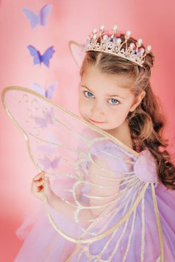 Taçlı ve kanatlı bir kızın utangaç bir gülümsemeyle poz vermesi.