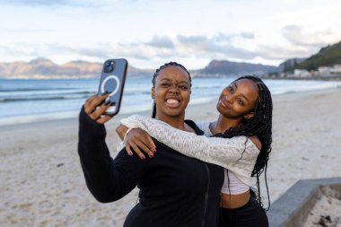 Arkadaşlar gün doğumunda sahilde selfie çekiyorlar.