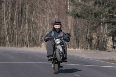15 yaşında, kasklı bir çocuk kırsal yolda motosikletini sürüyor.