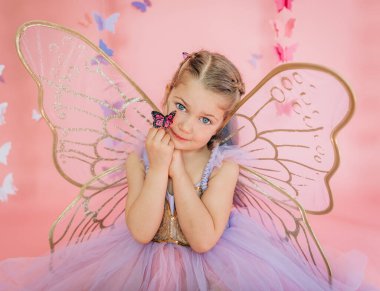 Peri kanatlı kız pembe arka planda pembe kelebek tutuyor.